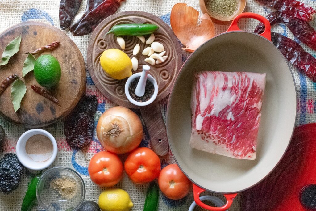 the authentic ingredients required to prepare the traditional Mexican dish, Birria de Res. This image captures the rich diversity of spices, herbs, and raw meat that come together in this beloved recipe, making it an ideal choice for culinary enthusiasts and food bloggers searching for genuine Mexican culinary content. Perfect for articles, blogs, or projects centered around Mexican cuisine, recipes, or cultural gastronomy.